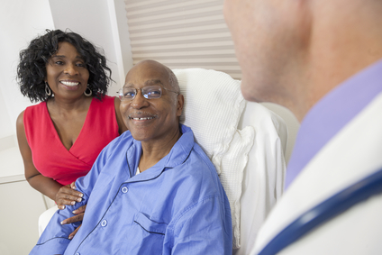 Happy senior African American man patient recovering in hospital bed with male doctor and wife